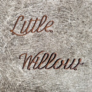 May include: Close-up of a rustic, gray surface with the words "Little Willow" written in rusty metal letters.