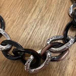 May include: A black and brown chain necklace with silver links. The links have a swirl design.