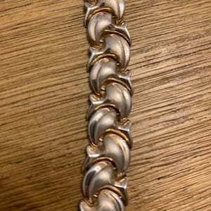 May include: A silver and gold bracelet with a twisted design. The bracelet is made of metal links that are interlocked.