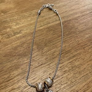 Pu&ograve; includere: Una collana a catena d'argento con tre perline d'argento e oro e un ciondolo a forma di cuore d'argento con strass trasparenti.