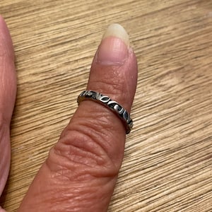 May include: A silver ring with a decorative design of small circles and ovals.