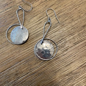 May include: A pair of silver earrings with a hammered circle design. The earrings have a simple wire loop design.