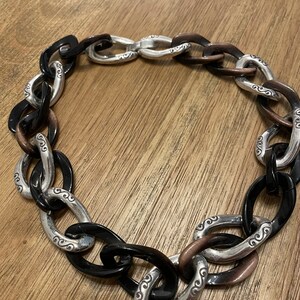 May include: A black and silver chain necklace with a chunky link design. The links are oval shaped and have a decorative pattern.