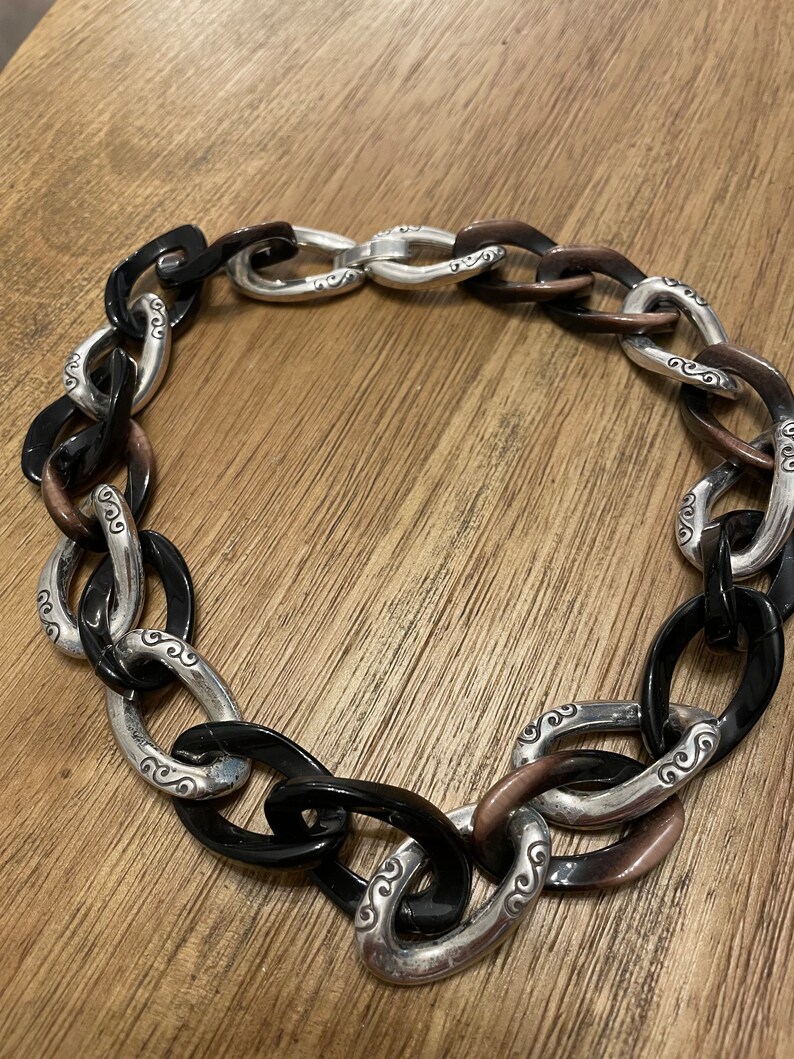 May include: A black and silver chain necklace with a chunky link design. The links are oval shaped and have a decorative pattern.