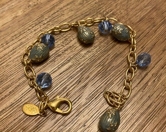 May include: A gold chain bracelet with blue and green glass beads. The beads are shaped like eggs and have a floral design. The bracelet has a lobster clasp.