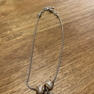 Pu&ograve; includere: Una collana a catena d'argento con un ciondolo a forma di cuore d'argento e oro e due ciondoli a forma di perla d'argento e oro.