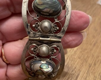 May include: A silver bracelet with an intricate design and three abalone shell inlays. The bracelet is hinged and opens to fit the wrist.