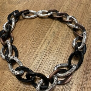 May include: A black and brown chain necklace with silver links. The links have a decorative swirl design.