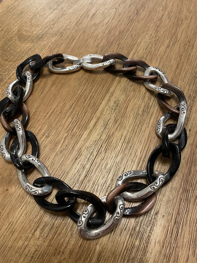May include: A black and brown chain necklace with silver links. The links have a decorative swirl design.