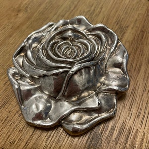 May include: A silver-colored rose-shaped trinket box. The rose is detailed and has a realistic appearance.