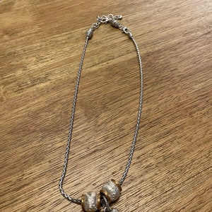Pu&ograve; includere: Una collana a catena d'argento con un ciondolo a forma di cuore d'argento e oro e due ciondoli a forma di perla d'argento e oro.