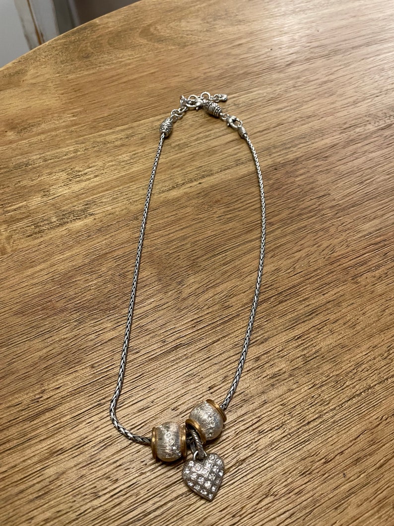 Pu&ograve; includere: Una collana a catena d'argento con un ciondolo a forma di cuore d'argento e oro e due ciondoli a forma di perla d'argento e oro.