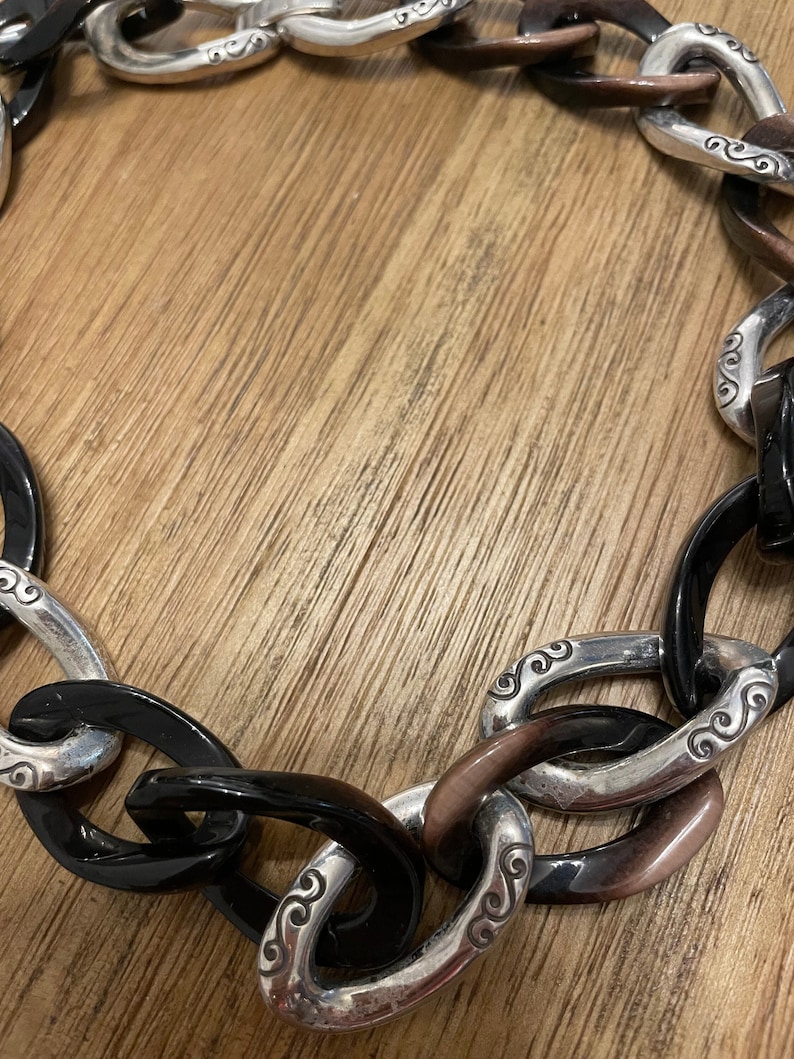 May include: A black and brown chain necklace with silver links. The links have a swirl design.