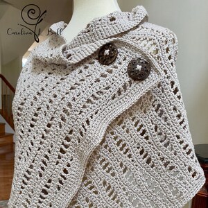 May include: A beige, open-weave crochet shawl with a collar and two large, round, wooden buttons. The shawl is draped over a mannequin. The text "Carolina L. Ball" is in the upper left corner.