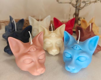 Puede incluir: Un conjunto de nueve velas con forma de gato, cada una de un color diferente y un tercer ojo en la frente. Las velas están hechas de cera y tienen un diseño realista de cara de gato.