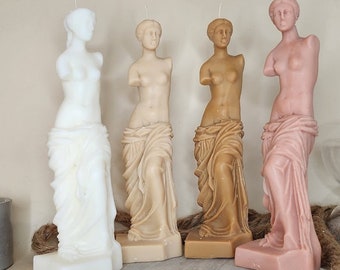 Op de afbeelding: Vier decoratieve kaarsen in de vorm van het standbeeld van de Venus van Milo. De kaarsen zijn in verschillende kleuren: wit, beige, bruin en roze.