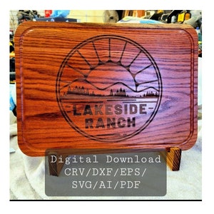 May include: A wooden cutting board with a laser-engraved design of a sun setting over a lake with trees. The design includes the text "LAKESIDE RANCH". The cutting board is on a small wooden stand. Digital Download: CRV/DXF/EPS/SVG/AI/PDF