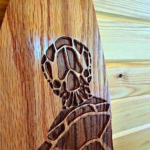 May include: A wooden paddle with a carved sea turtle design. The turtle is intricately detailed and has a brown and light brown color scheme.
