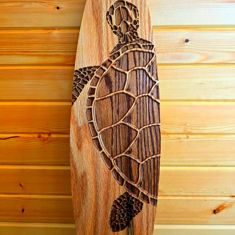 May include: A wooden surfboard with a carved sea turtle design. The turtle is brown and has a detailed shell.