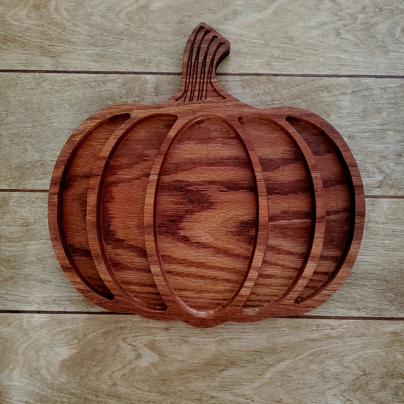 May include: A wooden pumpkin-shaped serving tray with four compartments. The tray is made of dark red wood with a natural wood grain.