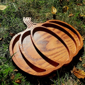May include: A wooden pumpkin-shaped serving tray with three separate compartments. The tray is made of light brown wood with a natural wood grain finish.