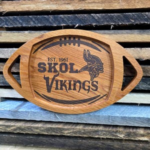 May include: A wooden serving tray shaped like a football with the Minnesota Vikings logo and the text "EST. 1961 SKOL VIKINGS".