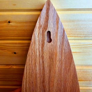 May include: A wooden plaque with a teardrop shape and a hole in the top for hanging. The plaque is made of a light brown wood with a natural grain pattern.