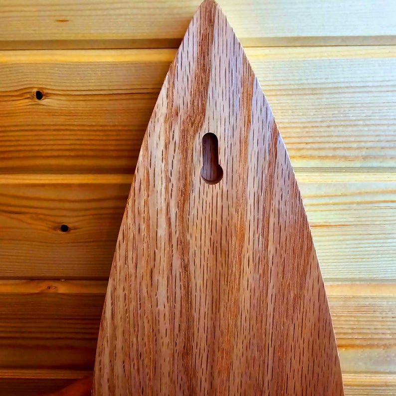 May include: A wooden plaque with a teardrop shape and a hole in the top for hanging. The plaque is made of a light brown wood with a natural grain pattern.