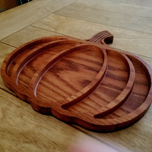 May include: A wooden pumpkin-shaped serving tray with three carved sections. The tray is made of dark brown wood with a natural grain pattern.