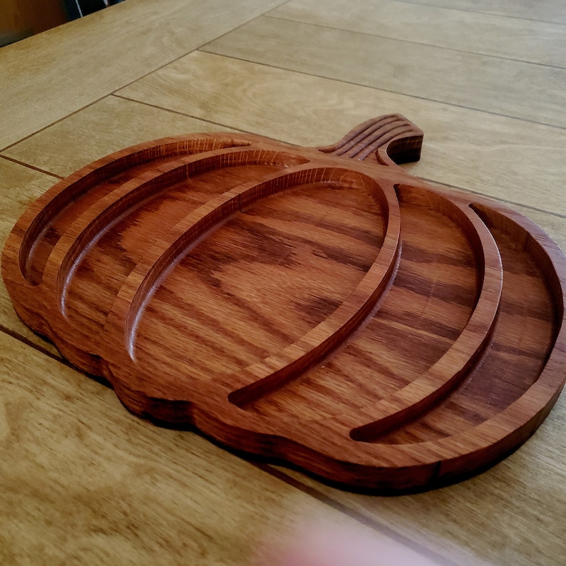 May include: A wooden pumpkin-shaped serving tray with three carved sections. The tray is made of dark brown wood with a natural grain pattern.