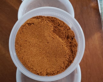 May include: A close-up of a clear plastic container filled with a brown spice powder. The container is sitting on top of another container.