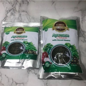 May include: Two silver pouches of Ayamase Sauce with locust beans. The pouches are labeled with the brand name "Blammode Top Favored" and the weight of the sauce, 500g and 1kg. The sauce is a dark green color and is ready to eat.