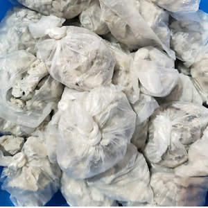 May include: A pile of small white bags filled with a white powdery substance. The bags are tied with a white string.