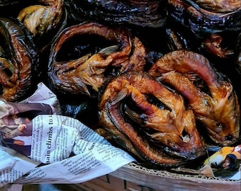 May include: A close-up of a box filled with smoked fish. The fish are arranged in a pile, with their dark brown and golden brown skin visible. The fish are arranged in a pile, with their dark brown and golden brown skin visible.
