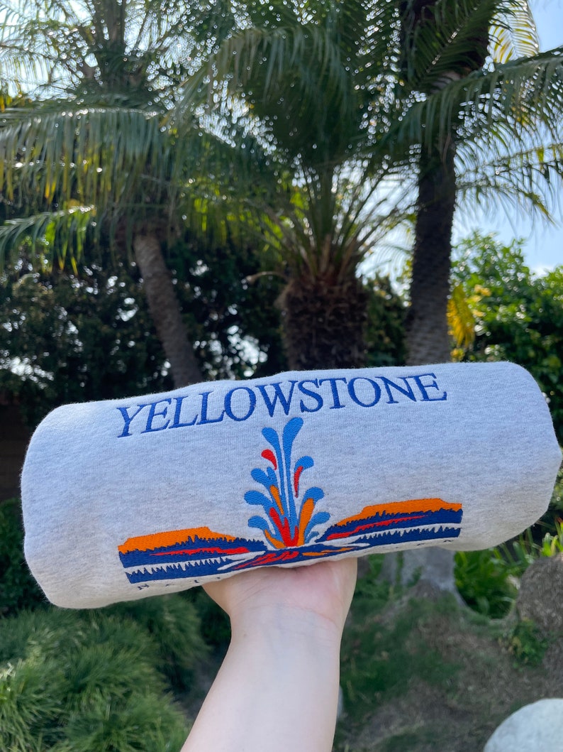 May include: Gray sweatshirt with a colorful graphic of a geyser and the text "Yellowstone National Park" printed on the front.