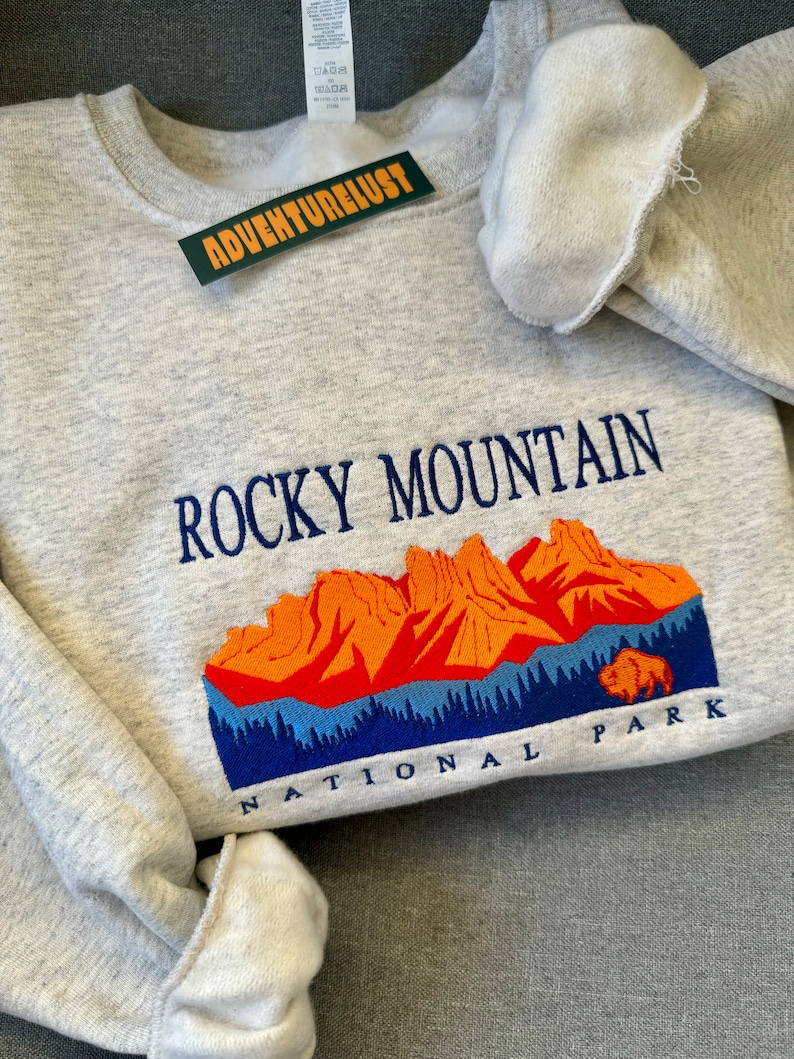 May include: Gray sweatshirt with embroidered text "Rocky Mountain National Park" and a graphic of a mountain range with a bison in the foreground.