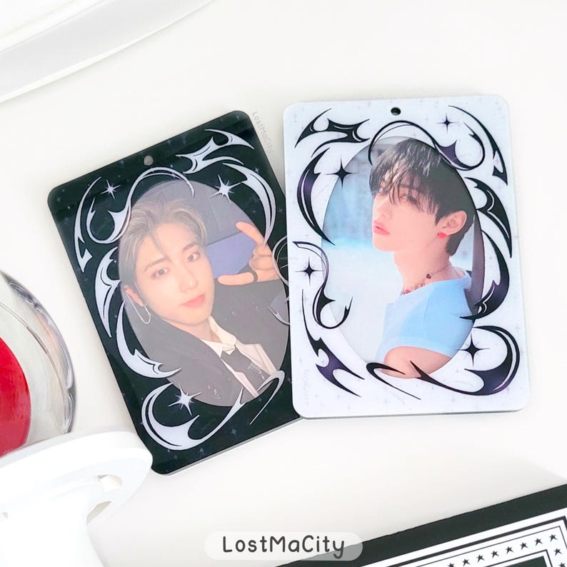 Puede incluir: Dos tarjetas fotogr&aacute;ficas rectangulares con im&aacute;genes de personas. Una tarjeta es negra con un borde decorativo blanco y negro, la otra es blanca con un borde similar. Las tarjetas tienen un acabado brillante. El texto "LostMaCity" es visible en la parte inferior.