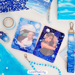 May include: A selection of blue and white accessories, including two photo card holders with images of people, a lanyard, washi tape, and stickers. The photo card holders feature a cloud and sun design. The lanyard has a blue and white cloud design.