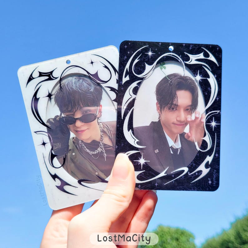 Puede incluir: Dos tarjetas fotogr&aacute;ficas rectangulares con im&aacute;genes de una persona. Una tarjeta es blanca con un borde decorativo en blanco y negro, la otra es negra con un borde blanco. Las tarjetas se sostienen contra un cielo azul. El texto "LostMaCity" es visible.