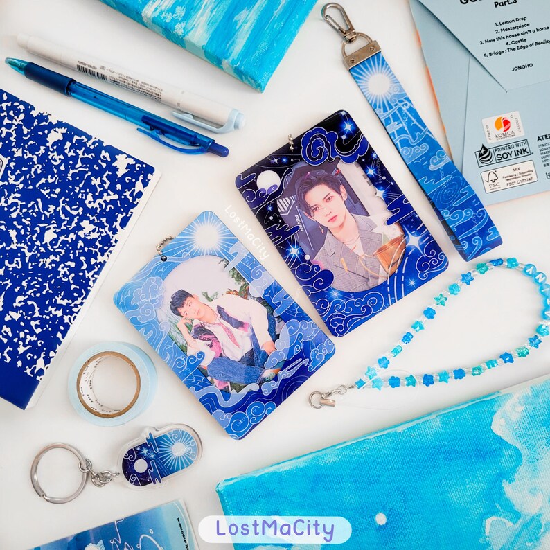 May include: A collection of blue and white stationery and accessories, including pens, notebooks, and a beaded lanyard. The image features photo cards with images of a person, a keychain, and a lanyard with a sun and cloud design. The text "LostMaCity" is visible.
