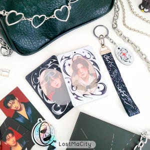 Puede incluir: La imagen muestra una colecci&oacute;n de productos. Se ven dos tarjetas rectangulares con retratos y bordes decorativos. Tambi&eacute;n hay un llavero con una correa estampada y un peque&ntilde;o dije. Una bolsa verde oscuro y cadenas plateadas est&aacute;n en el fondo. El texto "LostMaCity" es visible.