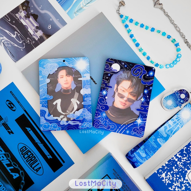 May include: A selection of blue and white merchandise, including photo cards, a bookmark, and a beaded phone strap. The items feature images of people and have a celestial theme with clouds and stars. The text "LostMaCity" is visible.