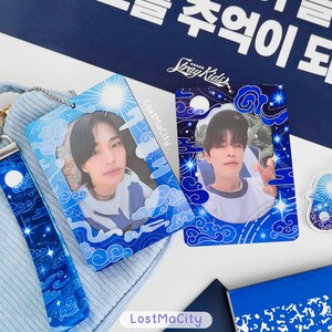 May include: Two blue photo cards with images of people, framed with a blue and white cloud and star design. They rest on a light blue surface, with a matching lanyard and a blue notebook visible.