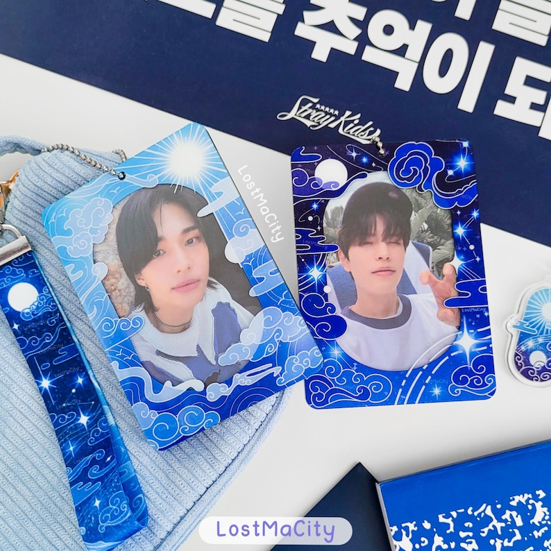 May include: Two blue photo cards with images of people, framed with a blue and white cloud and star design. They rest on a light blue surface, with a matching lanyard and a blue notebook visible.