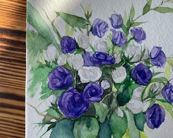 May include: Watercolor painting of a bouquet of roses in shades of purple and white. The flowers are surrounded by green leaves and stems. The artwork is on white paper, with a wooden surface in the background.
