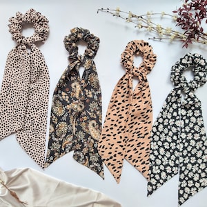 May include: Four hair scrunchies with long fabric ties. The scrunchies are in a variety of patterns, including black and white polka dots, paisley, black and white animal print, and white daisies on a black background.