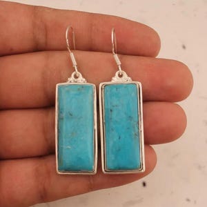 May include: A pair of silver dangle earrings featuring rectangular turquoise stones. The earrings have a simple design and are a classic style.