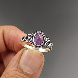 Könnte beinhalten: Ein silberner Ring mit einem ovalen Amethyst-Edelstein, der in einem dekorativen Filigranmuster gefasst ist.