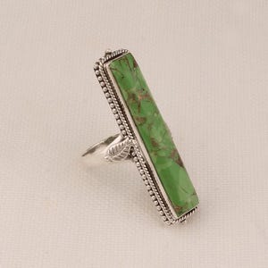Könnte beinhalten: Ein silberner Ring mit einem grünen Türkis-Stein, der in einer rechteckigen Fassung sitzt. Der Ring hat ein Perlenmuster um den Stein und ein Blattdesign am Band.