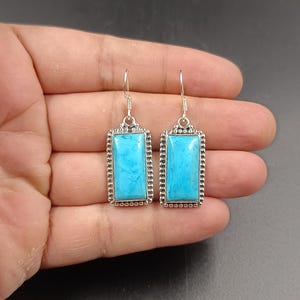 Puede incluir: Un par de pendientes de plata con piedras turquesa. Las piedras son rectangulares y de color azul claro.